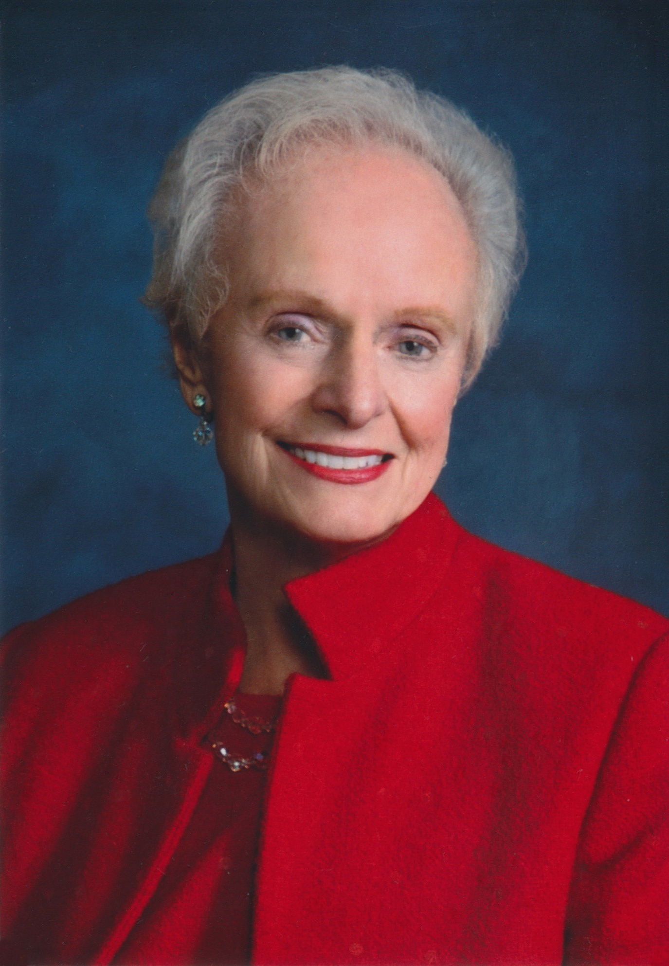 Portrait photo of Maggie Tinsman, an older white woman with white hair wearing a red coat.